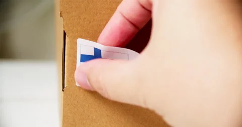 Hands applying MADE IN FINLAND  flag label on a shipping cardboard box Stock Footage 199571330