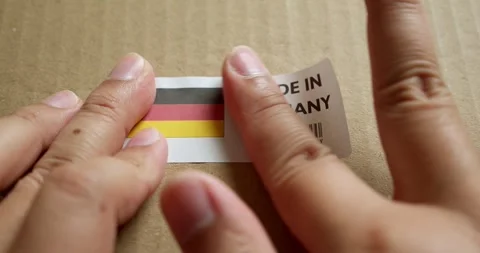 Hands applying MADE IN GERMANY flag label on a shipping box with product Stock Footage 253381638