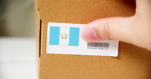 Hands applying MADE IN GUATEMALA flag label on a shipping cardboard box Stock Footage 200831769