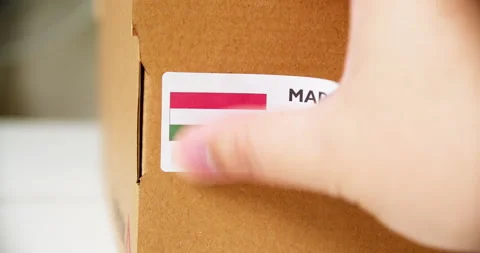 Hands applying MADE IN HUNGARY flag label on a shipping cardboard box with Stock Footage 201112004