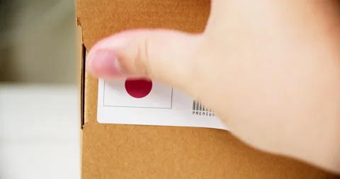 Hands applying MADE IN JAPAN flag label on a shipping cardboard box with Stock Footage 199009028