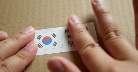 Hands applying MADE IN KOREA flag label on a shipping box with product Stock Footage 253384112