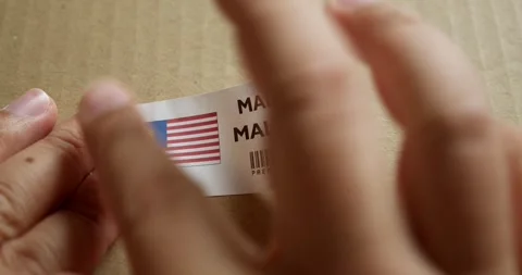 Hands applying MADE IN MALAYSIA flag label on a shipping box with product Stock Footage 254178857