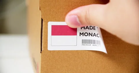 Hands applying MADE IN MONOCO flag label on a shipping cardboard box with Stock Footage 199237699