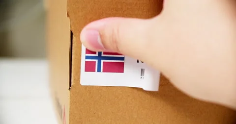 Hands applying MADE IN NORWAY flag label on a shipping cardboard box with Stock Footage 200499797
