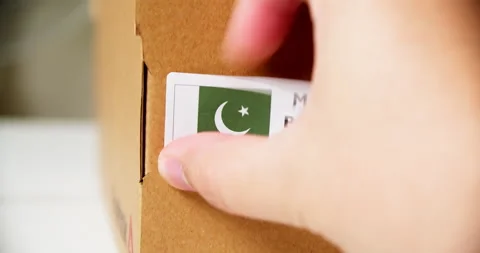 Hands applying MADE IN PAKISTAN flag label on a shipping cardboard box Stock Footage 201019358