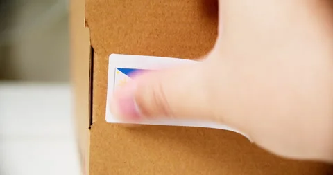 Hands applying MADE IN PHILIPPINES flag label on a shipping cardboard box Stock Footage 201019372