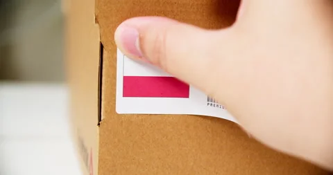 Hands applying MADE IN POLAND flag label on a shipping cardboard box with Stock Footage 200499998
