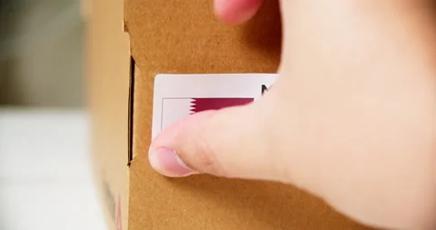 Hands applying MADE IN  QATAR flag label on a shipping cardboard box with Stock Footage 199009071