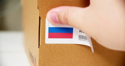 Hands applying MADE IN RUSSIA flag label on a shipping cardboard box with Stock Footage 199377941