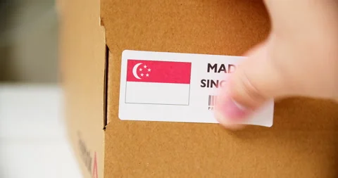 Hands applying MADE IN SINGAPORE flag label on a shipping cardboard box Stock Footage 200499692
