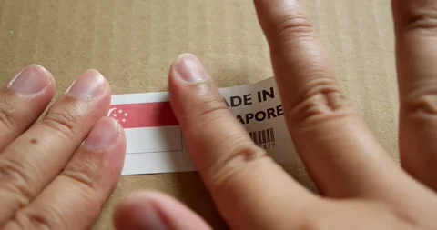 Hands applying MADE IN SINGAPORE flag label on a shipping box with product Stock Footage 254180750