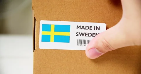 Hands applying MADE IN SWEDEN flag label on a shipping cardboard box with Stock Footage 199377895