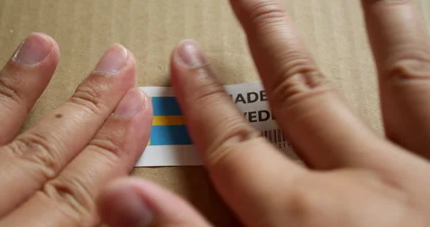 Hands applying MADE IN SWEDEN flag label on a shipping box with product Stock Footage 254078839