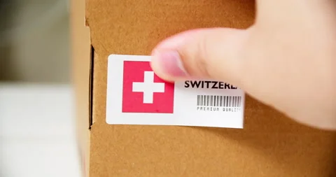 Hands applying MADE IN SWITZERLAND  flag label on a shipping cardboard box Stock Footage 199068559