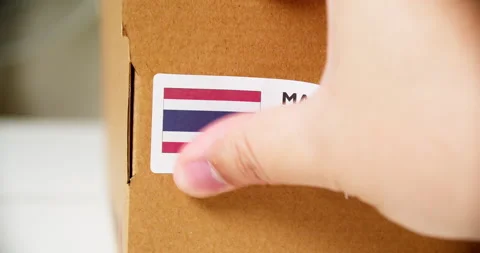 Hands applying MADE IN THAILAND flag label on a shipping cardboard box Stock Footage 199004711