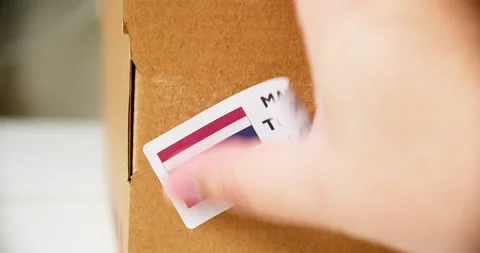 Hands applying MADE IN THAILAND flag label on a shipping cardboard box Stock Footage 200502349