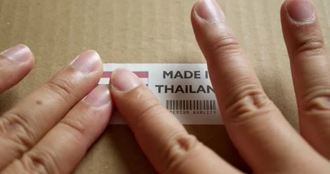 Hands applying MADE IN THAILAND flag label on a shipping box with product Stock Footage 253382860