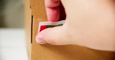 Hands applying MADE IN UAE flag label on a shipping cardboard box with Stock Footage 200498851