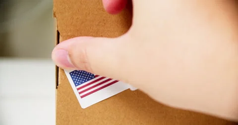 Hands applying MADE IN USA flag label on a shipping cardboard box with Stock Footage 200499896