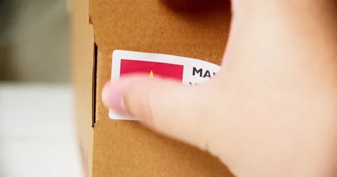 Hands applying MADE IN VIETNAM flag label on a shipping cardboard box with Stock Footage 199004673