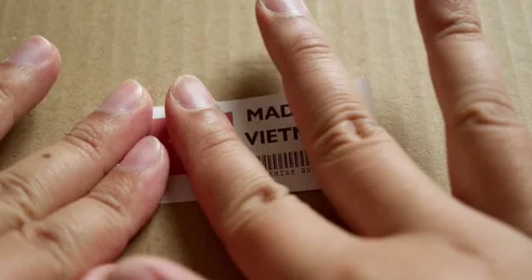 Hands applying MADE IN VIETNAM flag label on a shipping box with product Stock Footage 254105085