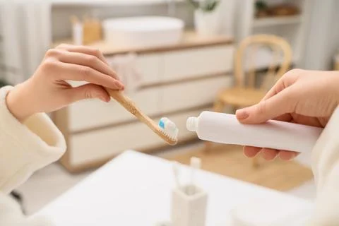 Hands applying toothpaste to a bamboo toothbrush in a bright bathroom, daily  Фото