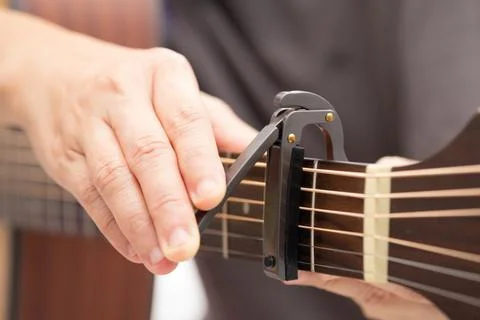 The hands are adjusting the capo to adjust the sound of the guitar. Stock Photos