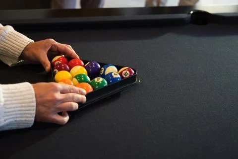 Hands are arranging black triangular rack filled with colorful billiard balls on Stock Photos