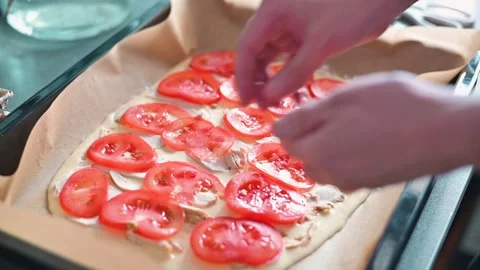Hands are arranging slices of fresh tomatoes on a flat dough base in a kitchen 動画素材 339096359