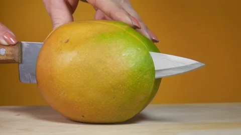 Hands are cutting a ripe mango with a knife on the yellow background Stock Footage 137630070