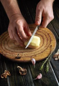Hands are holding a knife while cutting a potato on a round wooden board. Gar Stock Photos