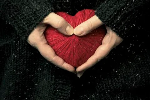 Hands are holding a red wool syrdze out of thread. Against a brown knitted sw Stock Photos