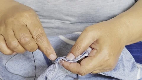 Hands are manually sewing patterned fabric using a needle and thread. Видео 347629396