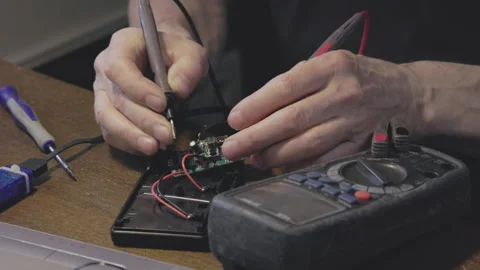 Hands are meticulously working with a multimeter and a detailed circuit board Stock Footage 306059577