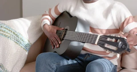 Hands are plucking strings and tuning pegs on black guitar on couch after 库存影片 343888818