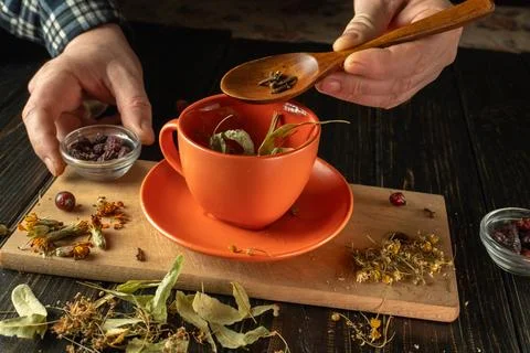 Hands are preparing herbal tea by adding dried leaves and spices into an or.. Stock Photos