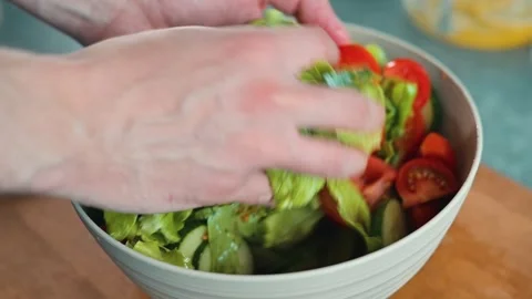 Hands are seen mixing fresh lettuce and tomatoes in a bowl. The setting is a Видео 338290405