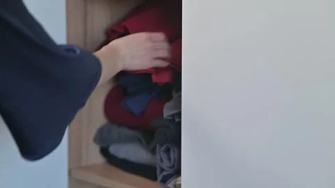 Hands are seen opening a storage cabinet and arranging folded clothes in a neat Видео 337555916