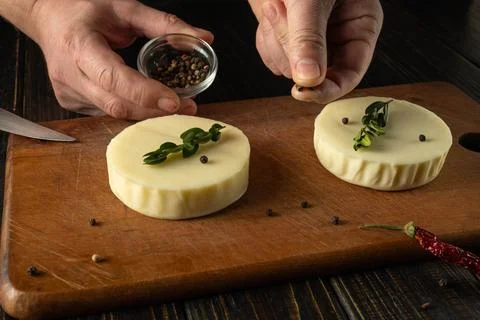 Hands are seen preparing cheese by adding peppercorns and herbs on a wooden.. Stock Photos
