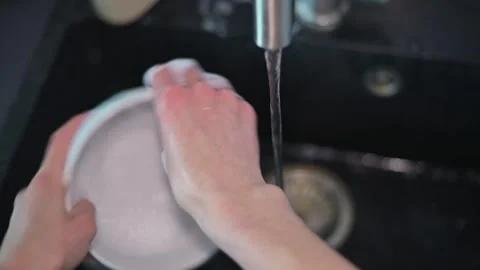 Hands are seen scrubbing and rinsing a bowl under running water in a kitchen Stock Footage 337642813