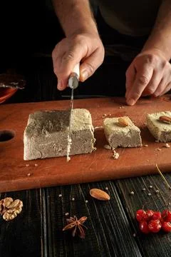 Hands are shown cutting a block of dessert made from nuts and spices on a w.. Stock Photos