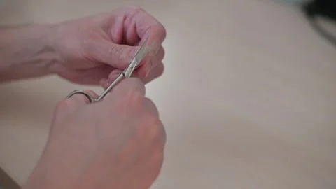 Hands are shown manipulating scissors to cut through an object on a flat surface 库存影片 337555810