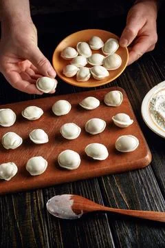Hands are skillfully shaping dumplings on a wooden table. Nearby, a plate h.. Stock Photos