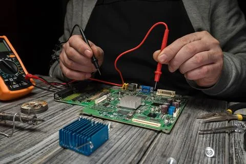 Hands are testing a circuit board with a multimeter. Tools like pliers and .. Stock Photos