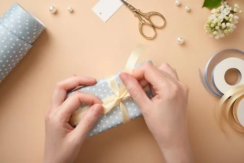 Hands are tying a bow on a light blue box. The process of wrapping a present. Stock Photos