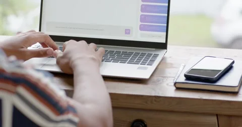 Hands are typing on laptop keyboard at wooden desk by window, prompted by Stock Footage 342954915