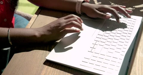 Hands are typing on light laptop at sunlit table as right hand is lowering for Stock Footage 335716000