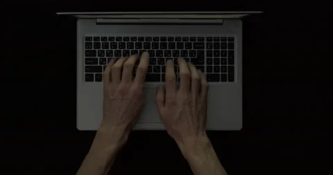 Hands are typing text on a laptop keyboard in a dark room. Top view. Stock Footage 147044466