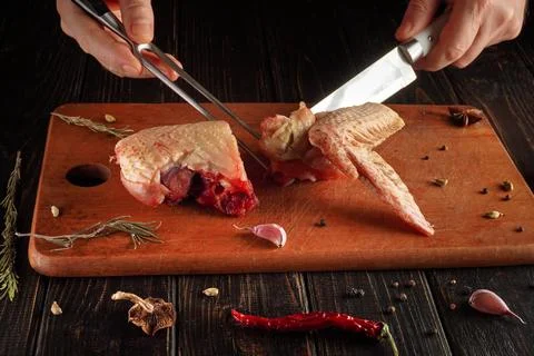 Hands are using scissors and a knife to cut raw meat on a wooden cutting boar Stock Photos